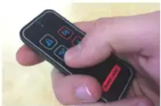 Close-up of a hand holding two remote control devices with function buttons (no readable text or symbols)