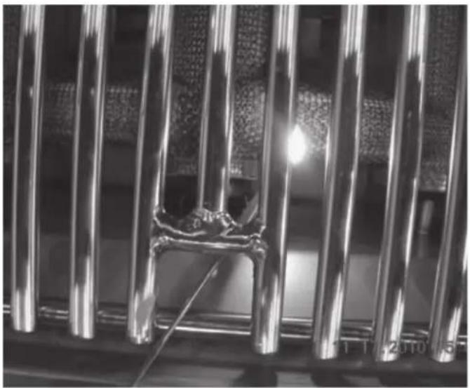 Close-up of metallic vertical bars with a small metal bracket and a light source, no visible text or symbols.