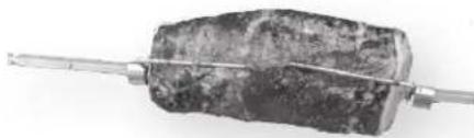 Close-up of a dark, irregularly shaped object with a metallic rod extending from its end (no visible text or symbols)