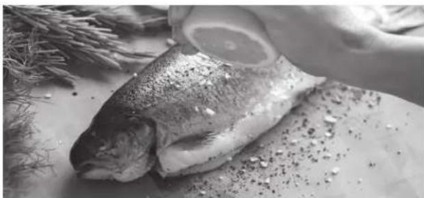 Black-and-white photo of a raw fish on a plate with herbs and rice in the background (no text or symbols visible)