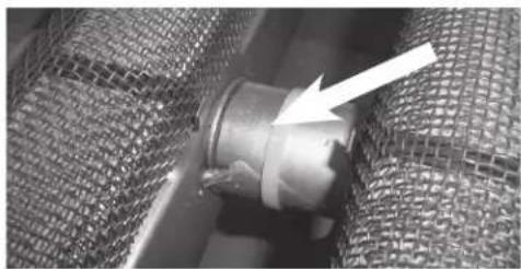 Close-up of a metallic pipe fitting with a white arrow pointing to it, partially enclosed in a mesh notebook (no text or symbols visible)