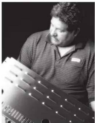 Black-and-white photo of a man examining a perforated metal component (no visible text or symbols).