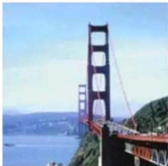 Exterior view of a large suspension bridge spanning a coastal landscape with hills and water.