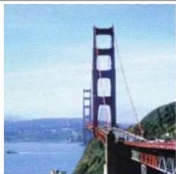 Exterior view of a large black suspension bridge spanning over water, with hills in the foreground.