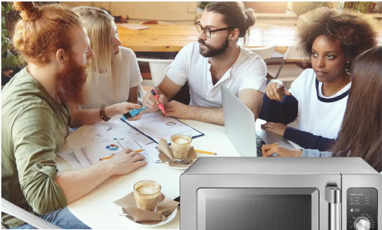 Groupe de quatre personnes en réunion autour d'une table avec des documents et un micro-ondes (aucun texte ou symbole visible)