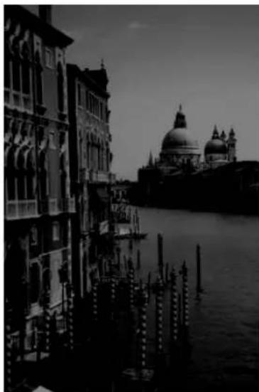 Black-and-white photo of a historic canal scene with Venetian-style buildings and a large domed building in the background (no visible text or symbols)