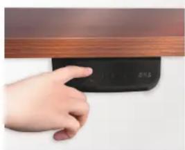Hand pressing a black electronic device with a display, against a wooden wall (no visible text or symbols)