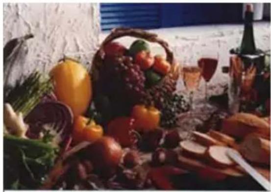 Still life photo of assorted fresh fruits and vegetables on a table, including a basket, glasses, and bread (no visible text or symbols)