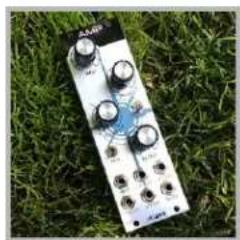 Close-up of a white electronic device with multiple knobs and control buttons, resting on green grass (no visible text or symbols)