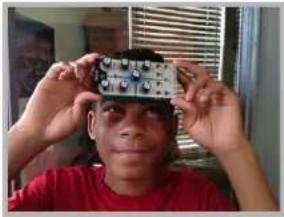 A young man in a red shirt adjusting a small electronic component on his head, with no visible text or symbols.