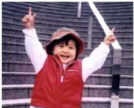 A smiling child in a red vest and hat standing on a staircase, making peace signs (no text visible)