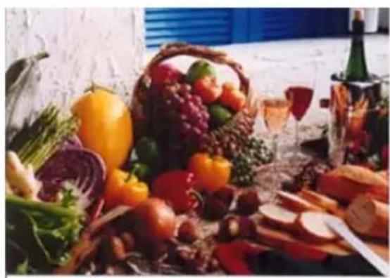 Assorted fresh vegetables and fruits including a basket, glasses, wine bottle, and bread slices (no visible text or labels)