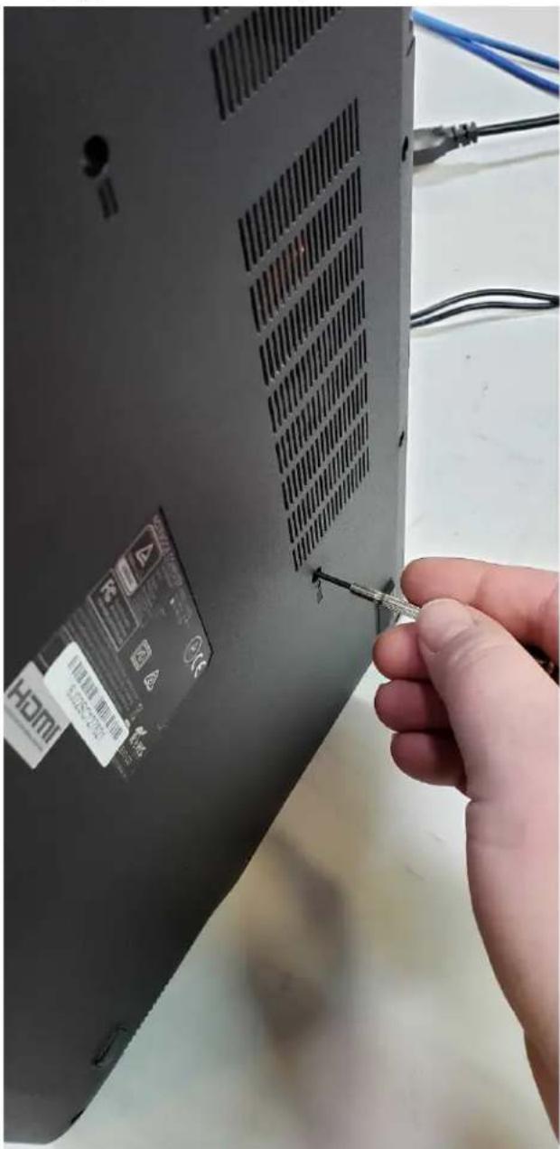 Hand inserting a screwdriver into a laptop cover with visible brand and product labels