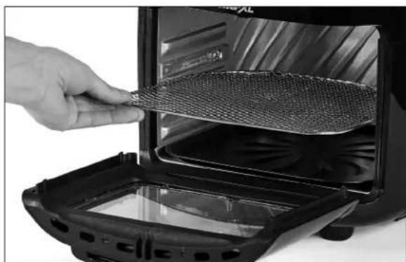 Close-up of a hand holding a textured food item inside an electric toaster oven (no visible text or symbols)
