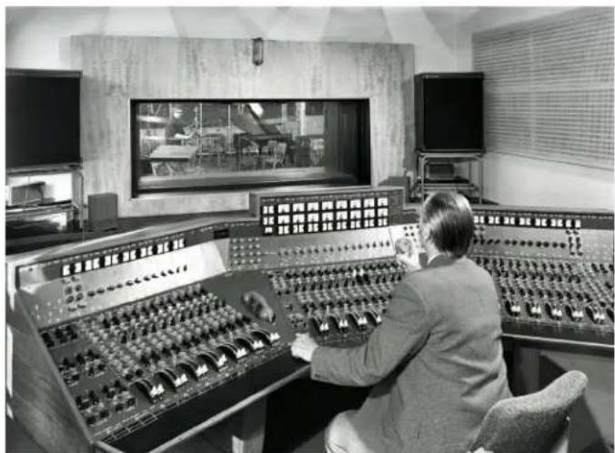 Interior of a vintage audio workstation with a person operating multiple audio equipment (no visible text or labels)