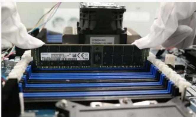 Close-up of gloved hands assembling a memory chip into a motherboard (no visible text or symbols)