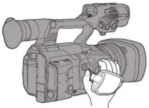 Line drawing of a professional video camera with a hand holding the lens (no text or symbols)
