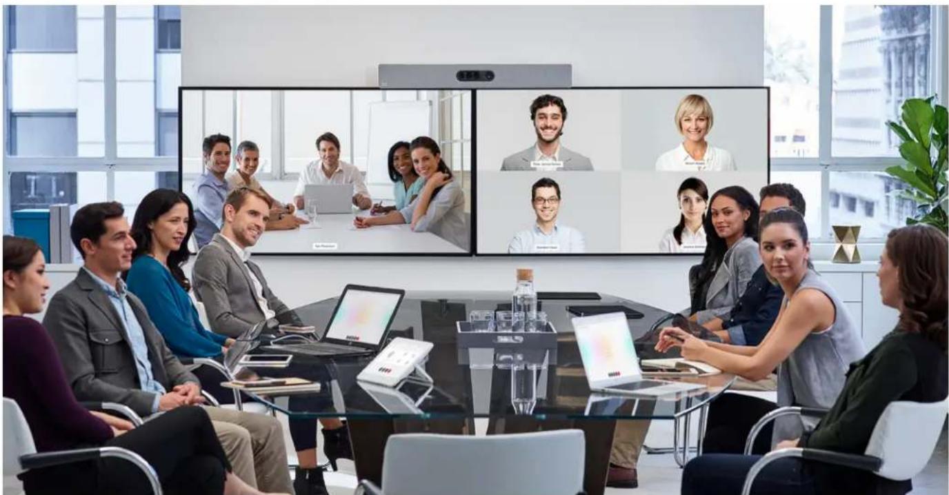 Business meeting in a modern office with participants seated around a table facing a large video call screen (no visible text or symbols)