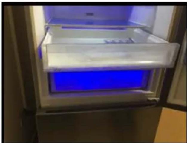 Interior view of a refrigerator with blue-lit storage panel (no visible text or symbols)