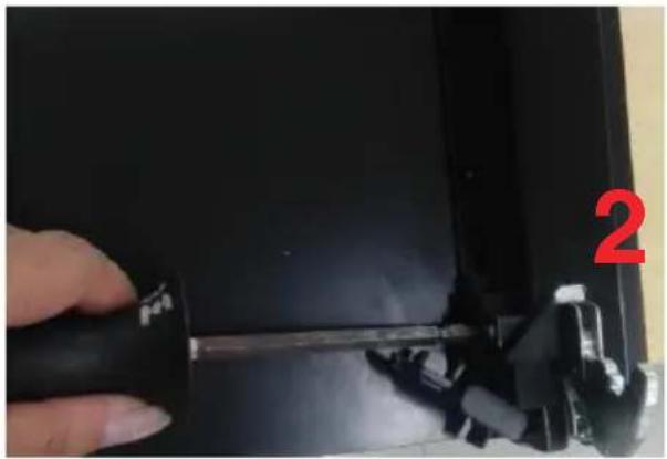 Close-up of a hand holding a black tool with a red number '2' on the right, next to a dark rectangular object (no readable text or symbols).
