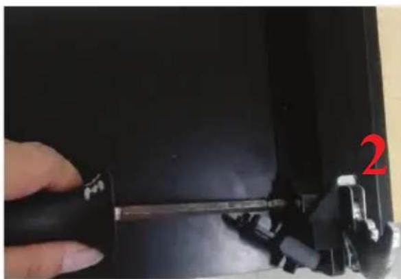 Close-up of a hand holding a tool inside a black electronic device, with a red number '2' visible on the right (no text or symbols on the device itself)