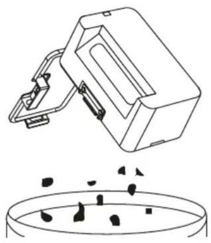 Line drawing of a mechanical device above a circular container with scattered black objects.