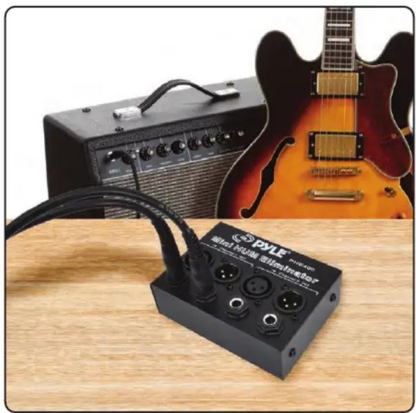Electronic audio amplifier connected to a black electronic device with three connectors, next to an acoustic guitar on a wooden table (no visible text or symbols)