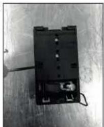 Black-and-white photo of an electronic device with a small component and wiring, placed on a wooden surface (no visible text or symbols)
