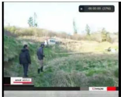Two people walking on a grassy hillside with a small building in the background (no visible text or symbols)