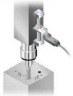 Close-up of a metal drill bit with a screw, mounted on a workbench (no visible text or symbols)