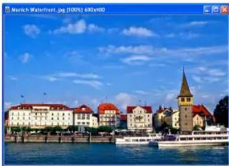 Scenic view of a historic European waterfront town with red-roofed buildings, a prominent church tower, and a boat on the water under a blue sky (no visible text or symbols)