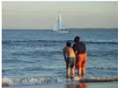 Three people standing by the sea with a sailboat on the horizon (no text or symbols visible)