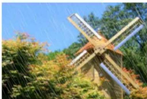 Wooden windmill in a forested area under clear blue sky (no text or symbols visible)