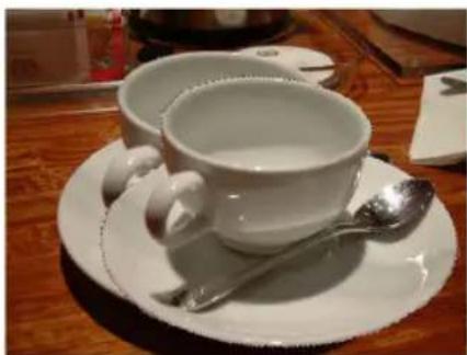 White ceramic teacup and saucer on a wooden table, with a spoon resting on the cup (no visible text or symbols)