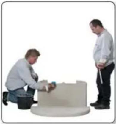 Two people working on a circular mechanical component, one kneeling and the other standing (no visible text or symbols)