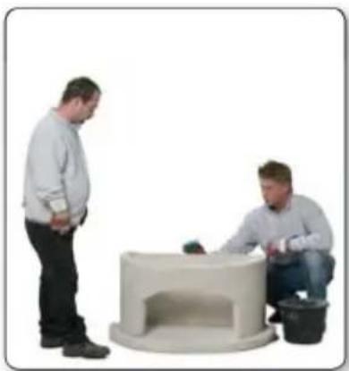 Two men interacting near a small white cylindrical device, one standing and one seated (no visible text or symbols)