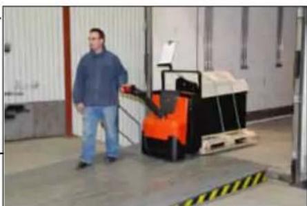 Interior view of a warehouse with a person standing beside an orange forklift and palletized goods (no visible text or symbols)