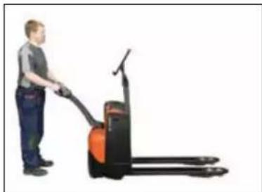 Person standing next to a hand-pulled automated pallet jack (no visible text or symbols)