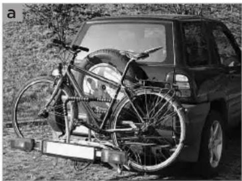 Black-and-white photo of a car with bicycles mounted on a vehicle chassis, outdoors (no visible text or symbols)