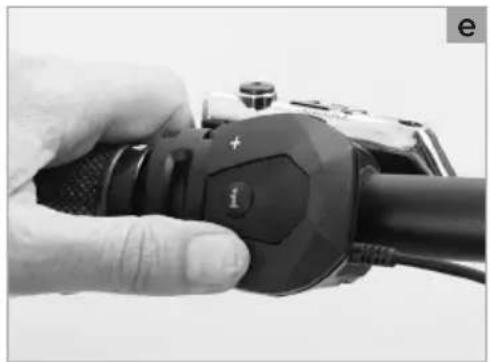 Close-up of a hand holding a black handheld device with a circular button and indicator lights (no visible text or symbols)