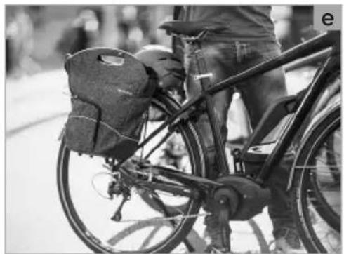 Black-and-white photo of a person riding a bicycle with a puffer bag (no visible text or symbols)