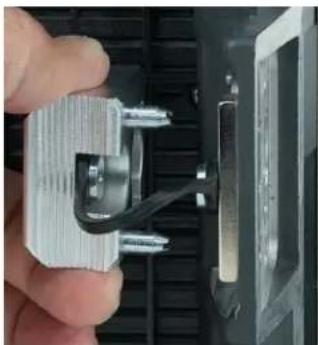Close-up of a hand holding a metallic electrical connector with wires, partially installed in a black plastic housing (no visible text or symbols)