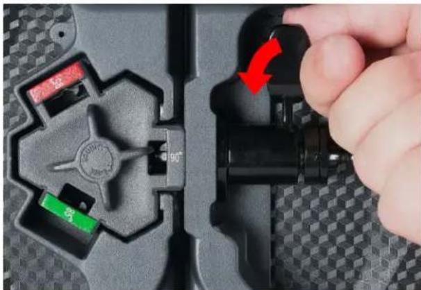 Close-up of a hand pressing a black mechanical component with a red arrow indicating rotation (no text or symbols visible)