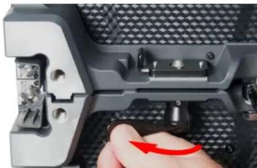 Close-up of a mechanical component with a hand adjusting a red arrow, showing internal parts and mounting holes (no text or symbols visible)