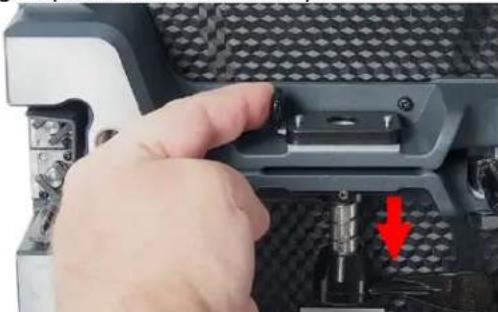 Close-up of a hand pressing a button on a mechanical component with a red arrow indicating a specific part (no text or symbols visible)