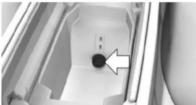 Interior view of a refrigerator with a circular button and an arrow pointing to it (no text or symbols visible)