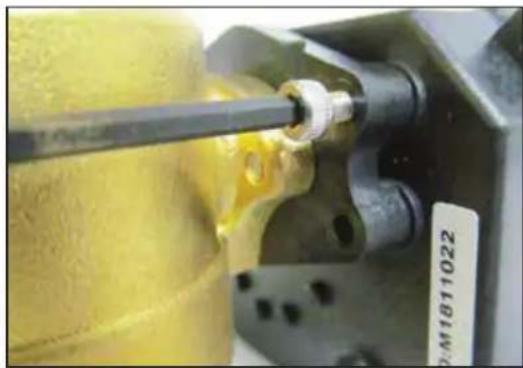 Close-up of a mechanical component with a yellow cylindrical part inserted, showing a tool and mounting holes (no visible text or symbols)