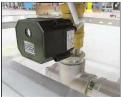 Close-up of a mechanical valve assembly with a green and black component, mounted on a metallic pipe (no visible text or symbols)