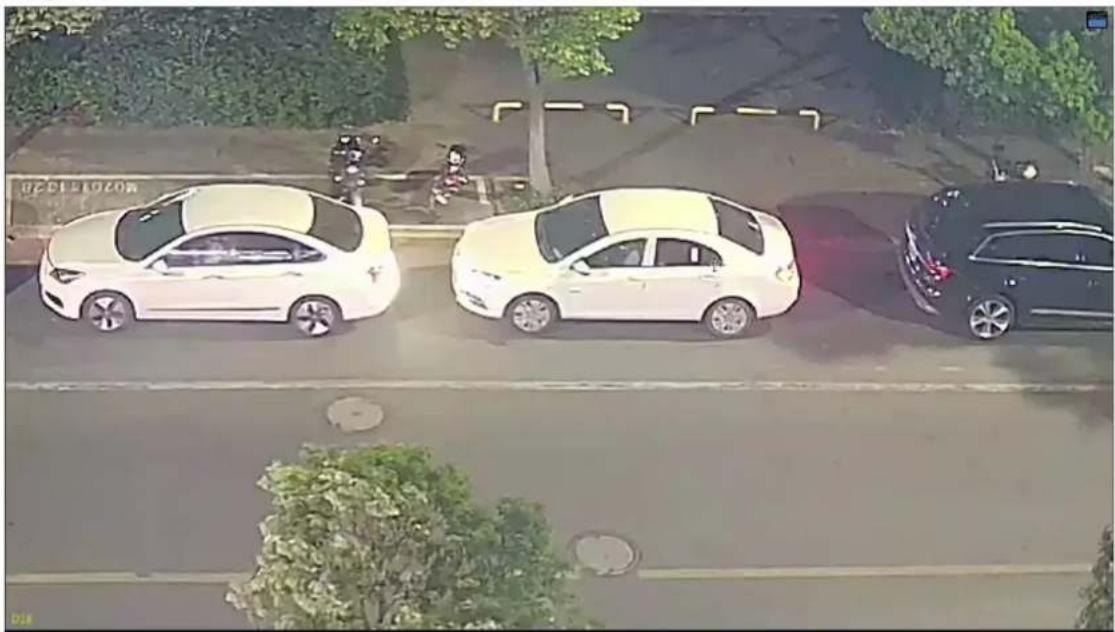 Aerial view of three cars parked on a wet road with trees and a paved area in the background (no visible text or symbols)