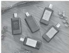 Five black spray bottles with visible labels, placed on a wooden surface with dried flowers (no text or symbols)